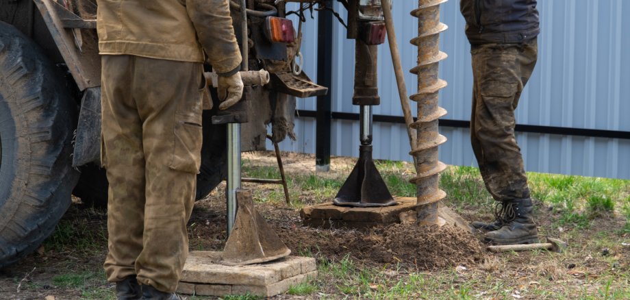 Team of workers with drilling rig on car are drilling artesian well for water in ground. Insertion of metal casing pipe into ground, installation of individual drinking supply