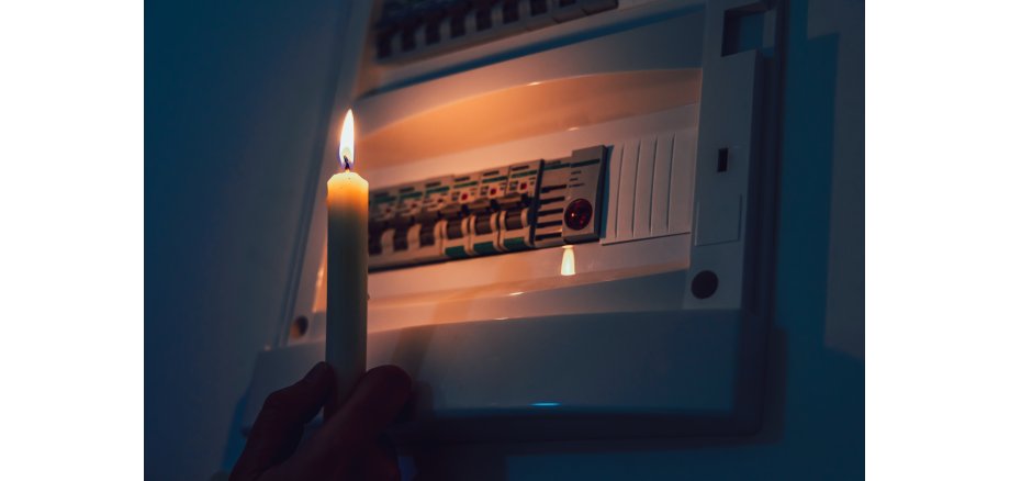 Energy crisis. Hand in complete darkness holding a candle to investigate a home fuse box during a power outage. Blackout concept. Energy crisis. Hand in complete darkness holding a candle to investigate a home fuse box during a power outage. Blackout concept.