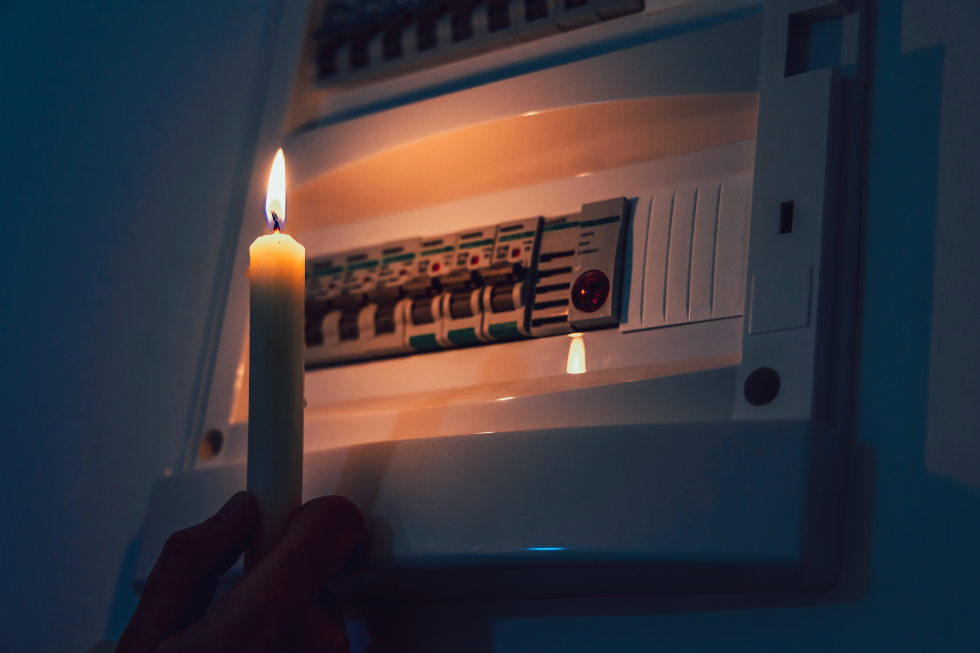 Energy crisis. Hand in complete darkness holding a candle to investigate a home fuse box during a power outage. Blackout concept.
